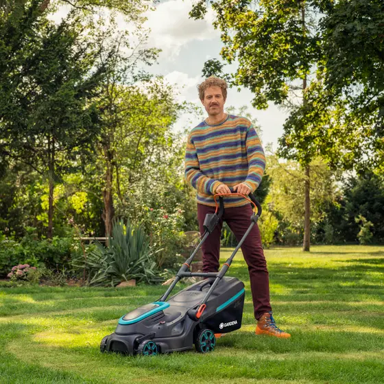 A man in the garden with a battery lawnmower